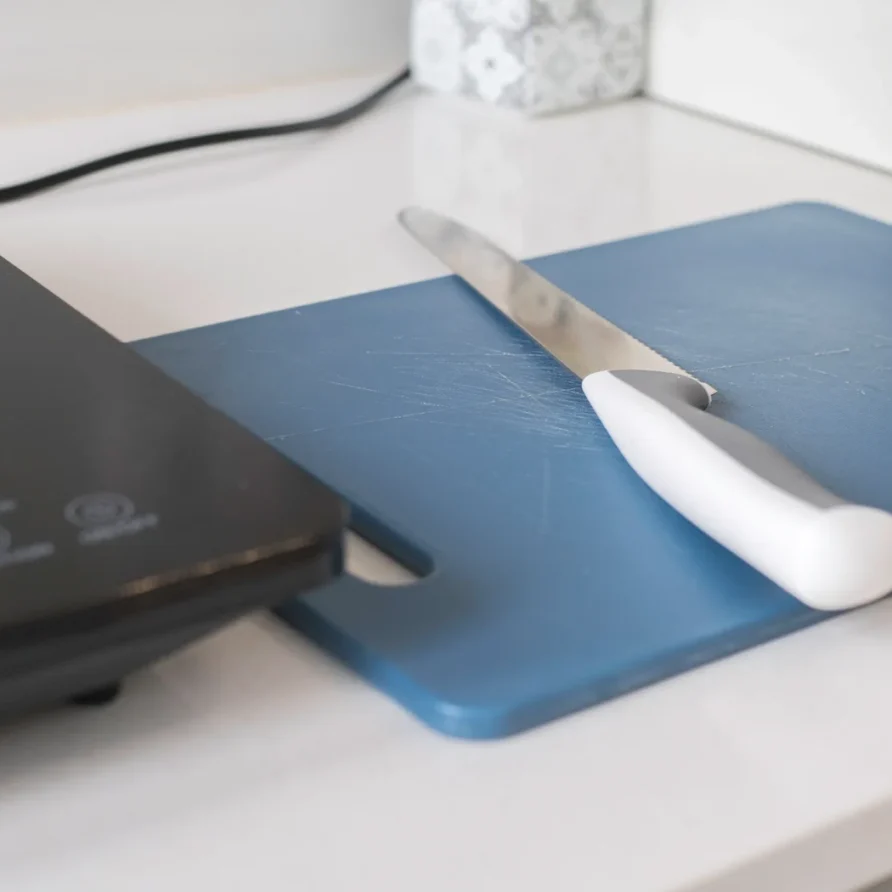 Knife on blue cutting board next to a black appliance
