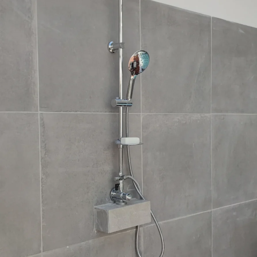 Chrome shower head and system on a gray tiled bathroom wall