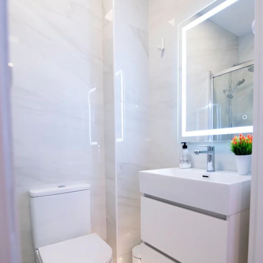 Modern white bathroom with toilet, vanity, and lighted mirror